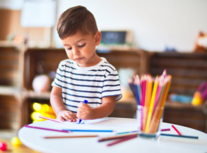 Beautiful toddler boy drawing cute draw using colored pencils at kindergarten